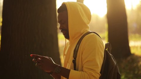 Happy young african american attractive man use smartphone walking in autumn park outside sunlight sunset street looking happy handsome boy cellphone mobile telephone outdoors close up slow motion: film stockowy