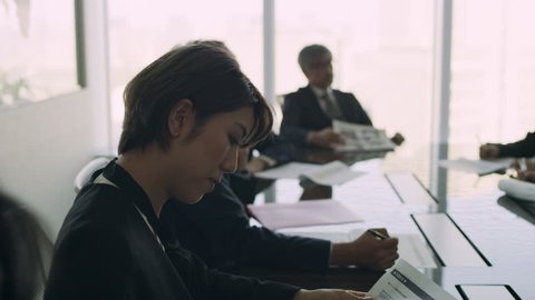 Medium shot on 4k RED camera. Group of Japanese business people work together in a meeting at a large conference room table in a modern office with soft natural lighting.
