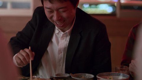 Content Japanese man eating tempura shrimp and talking with his friends on a boat with soft interior light. Close up shot on 4k RED camera.