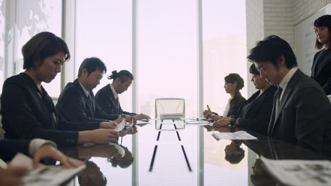 Medium shot on 4k RED camera. Group of Japanese business people are disappointed after boss sits down and delivers bad news in a small business office with soft natural lighting.