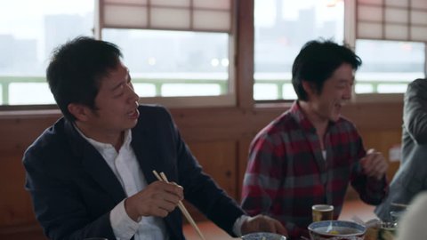 Group of happy Japanese friends sitting at a table drinking and eating on a boat with bright natural lighting in Fall. Medium shot on 4k RED camera on gimbal.
