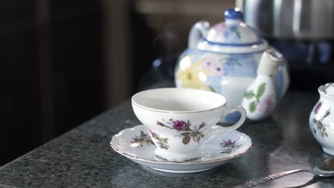 Close up of older person pouring tea from a colorful teapot into a china teacup and walking away with it.