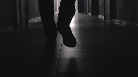 Dolly with low-section of silhouette of legs of man walking along hallway towards the camera