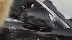 Person cleaning the car of snow after heavy snowfall, brushing it off with soft tool, viewed in close-up