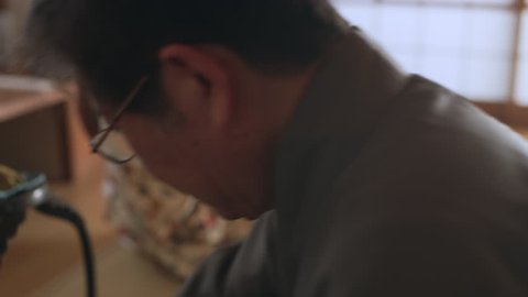 Accomplished tea maker adding powdered matcha tea to a bowl in a traditional Japanese home with soft day lighting. Close up shot on 4k RED camera.