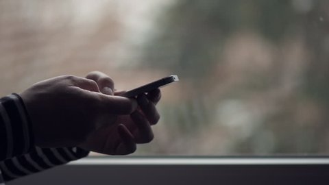 Woman using mobile phone for text messaging by the window, dolly slider shot