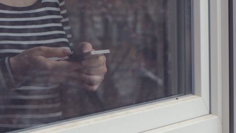 Woman using mobile phone for text messaging by the window