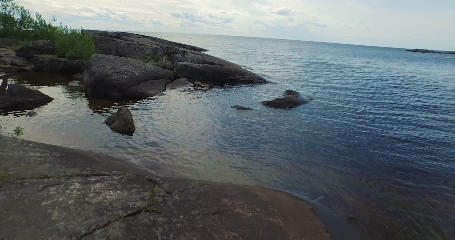 fast flight above bare rocks on lake bank under overcast sky