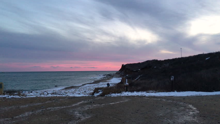 Lone person walks by the shoreline at Montauk Point State Park Beach during sunset in the hamlet of Montauk in the Town of East Hampton in Suffolk County, New York.