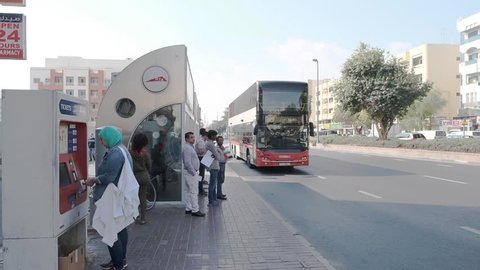 DUBAI/UNITED ARAB EMIRATES - JANUARY 05 2019: People stand at Dubai bus stop with air conditioning and large modern tourist double-decker bus passes along street on January 05 in Dubai