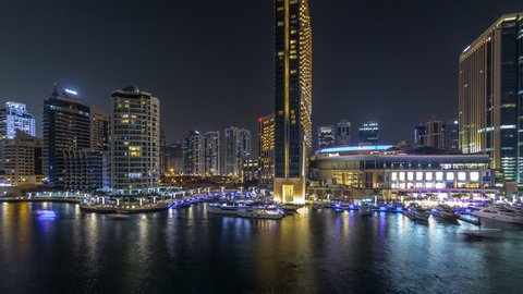 Aerial vew of Dubai Marina with shoping mall, restaurants, towers and yachts night timelapse, United Arab Emirates. Top view of canal with illuminated buildings and waterfront