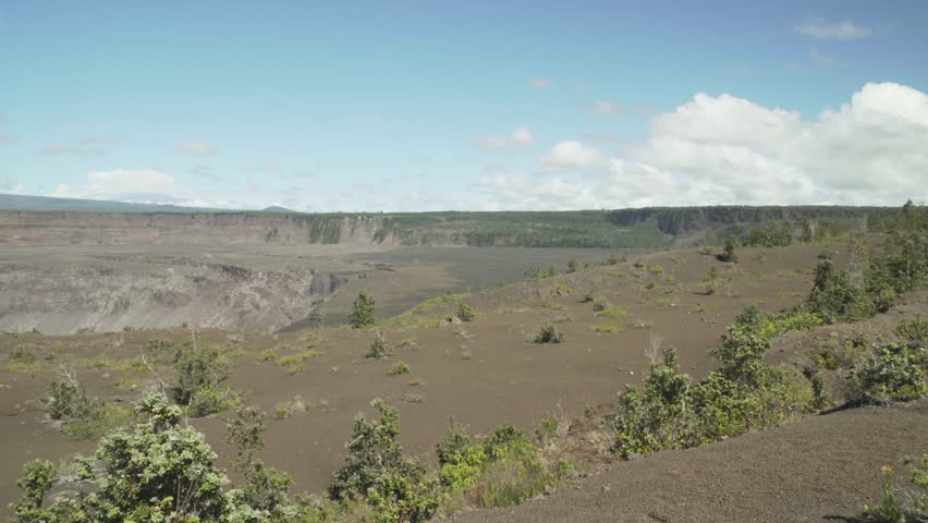 Right to left pan of volcano crater with dead trees and lava rocks on the ground and steam and smoke coming out of the ground