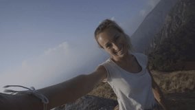 Cheerful young woman taking a selfie portrait on mountain top after hiking all the way up reaching summit