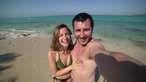 handsome cheerful young couple in love taking selfie on beach. Portrait of carefree tourists enjoying summer vacation. Happy couple on perfect white sand beach on travel holidays.