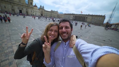 Happy young couple travelling in Colombia taking a selfie photo in the capital Bogota, smiling in the main square Bolivar in Calendaria district