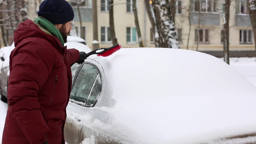 Man cleaning snow from car with brush