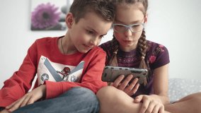 Portrait of kids looking at mobile phone at home. Sister and brother playing video games on mobile phone. Children looking gadget