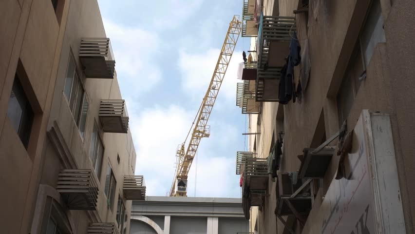 low angle shot from between houses in narrow street large building crane operates against blue sky with white clouds