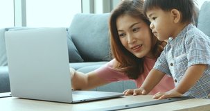Asian mother and son sitting in living room, they using notebook to watch some video, concept for mother and son using laptop