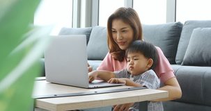 Asian mother and son sitting in living room, they using notebook to watch some video, concept for mother and son using laptop