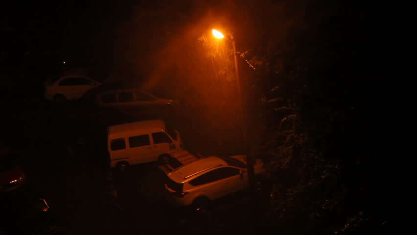 Silhouettes of cars on the parking in lights of street lantern lamp in night downpour