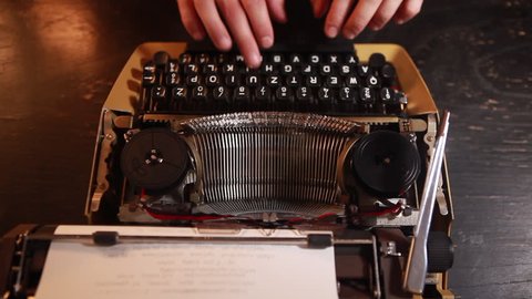 Writing a book on an old typewriter. Man's fingers are typing on the keyboard.
