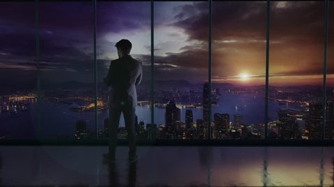 Silhouette of the businessman in the office standing in front of a big window with a view of Hong Kong. Talking on a phone and discussing business
