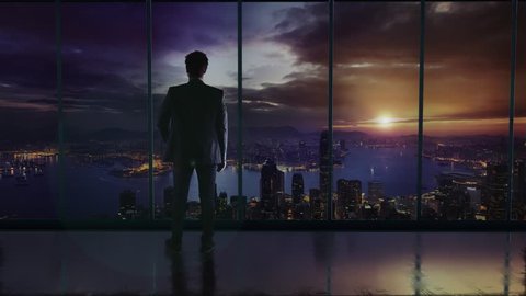 Silhouette of the businessman in the office standing in front of a big window with a view of Hong Kong. Talking on a phone and discussing business