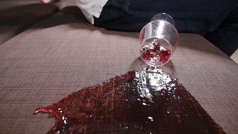A glass of wine falls on the sofa and spills wine.