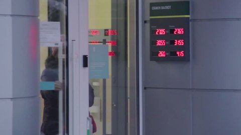 DNIPRO, UKRAINE - December 27, 2018: An elderly woman comes out of the doors of the Oschadbank branch. Glowing sign with currency exchange rate of dollars and euros in relation to Ukrainian hryvnia
