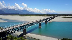 Aerial view of road bridge across the blue river with mountain scenery in summer of West Coast in South island, New Zealand. 4K video taken from drone.