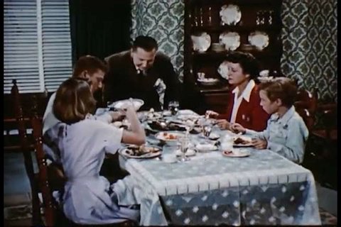 CIRCA 1950s - A family sits down and eats at a dinner table in a dining room in a home.