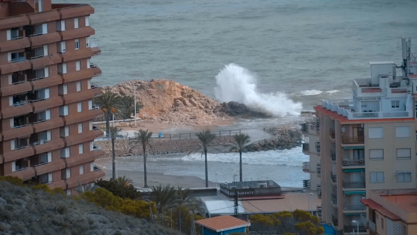 Stormy sea with big blue waves with foam whitecaps and splashes are break on coastal rocks near of the hotels. Slow mo, slo mo, slow motion, high speed camera, 240fps, 250fps