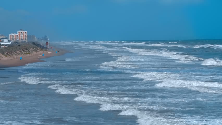 Stormy sea with big blue waves with foam whitecaps and splashes on the background of the coastal city. Slow mo, slo mo, slow motion, high speed camera, 240fps, 250fps
