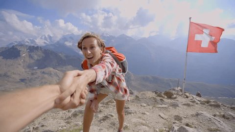 Hiker assisting teammate at mountain top giving a helping hand to reach summit, Switzerland.