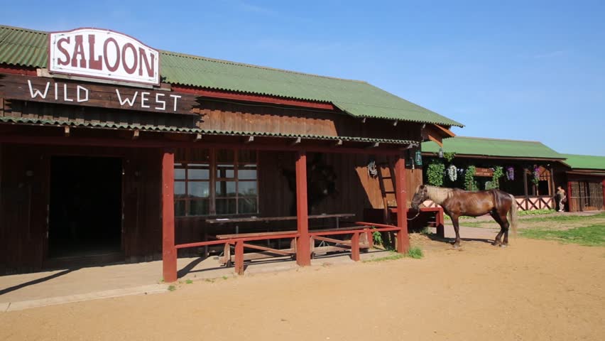Wild West saloon building, made of wood with a horse tied at feeding trough.