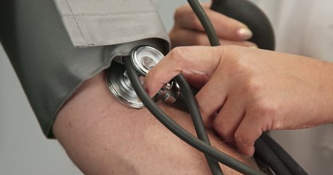 Extreme close up on stethoscope and blood pressure cuff on arm as doctor checks older male patient using sphygmomanometer. Slow motion 4k