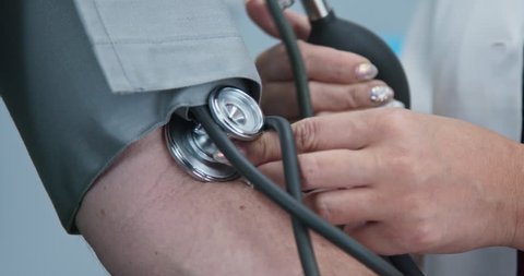 Extreme close up on stethoscope and blood pressure cuff on arm as doctor checks older male patient. Rack focus to pumping bulb to inflate sphygmomanometer. Slow motion 4k