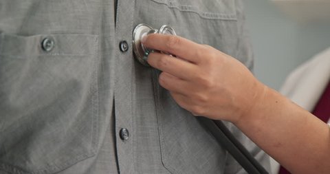Extreme close up on hands of doctor placing stethoscope on chest of male patient to hear heart rate and breathing. Slow motion 4k