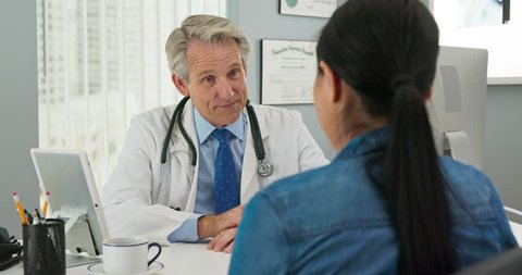Mature Caucasian male doctor in his office listening to new patient and smiling. Primary care physician going over medical history with Japanese woman. Slow motion 4k