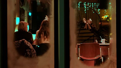 Girl friends sitting in night restaurant on Christmas Eve, view through window