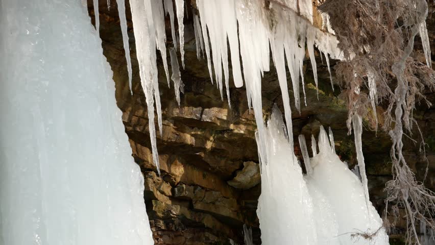 Low angle view of the mostly frozen Wequiock Falls near Green Bay, Wisconsin with large, frozen icicles and water flowing.