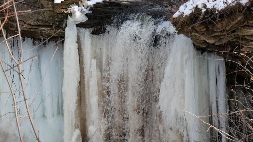 Low angle view of the mostly frozen Wequiock Falls near Green Bay, Wisconsin with large, frozen icicles and water flowing.