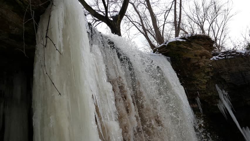 Low angle view of the mostly frozen Wequiock Falls near Green Bay, Wisconsin with large, frozen icicles and water flowing.