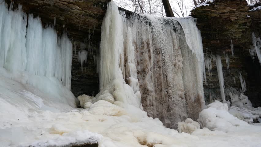 Low angle view of the mostly frozen Wequiock Falls near Green Bay, Wisconsin with large, frozen icicles and water flowing.