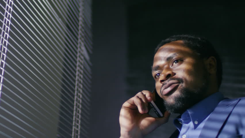 Low angle view of black male entrepreneur in formal clothes standing by office window and having telephone conversation