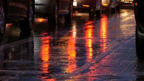 Cars stand in traffic, headlights in the rain on asphalt, view below. Rain hits the puddles at night. Reflection of car's lights