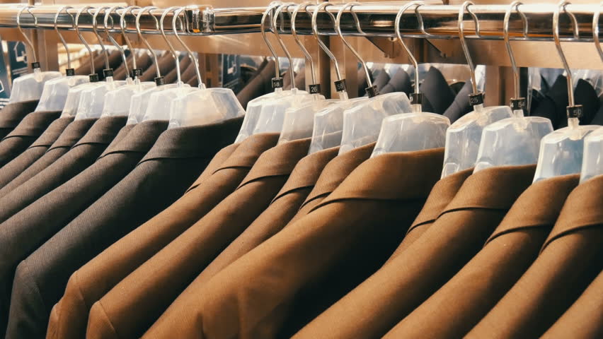 Brown and gray men's jackets hang on hangers in the men's clothing store in the mall. A huge range of men's suits on hangers in the shopping center close up view | Shutterstock HD Video #1022245999