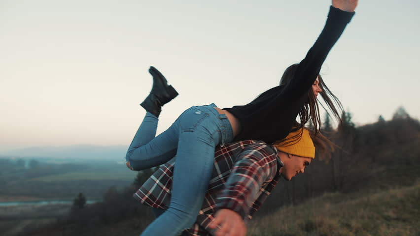 Young couple in love on vacations enjoying mountains. Attractive man is carrying girlfriend on his shoulders and whirls her. Having fun