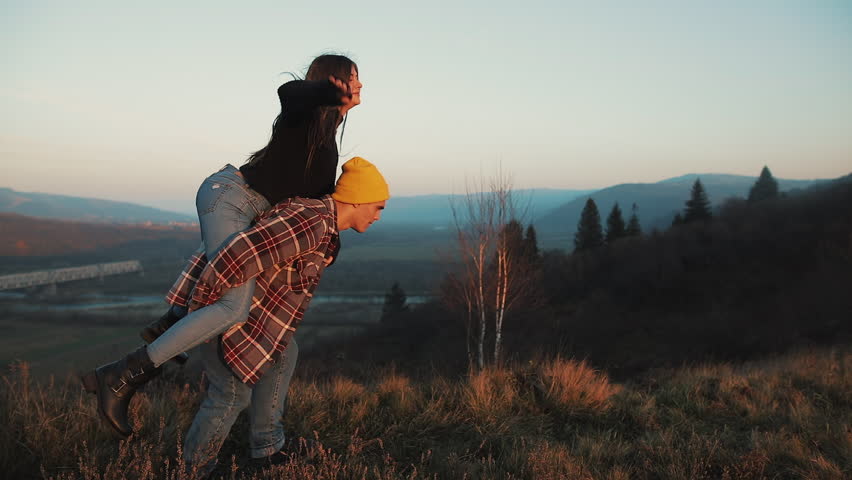 Young couple in love on vacations enjoying mountains. Attractive man is carrying girlfriend on his shoulders and whirls her. Having fun